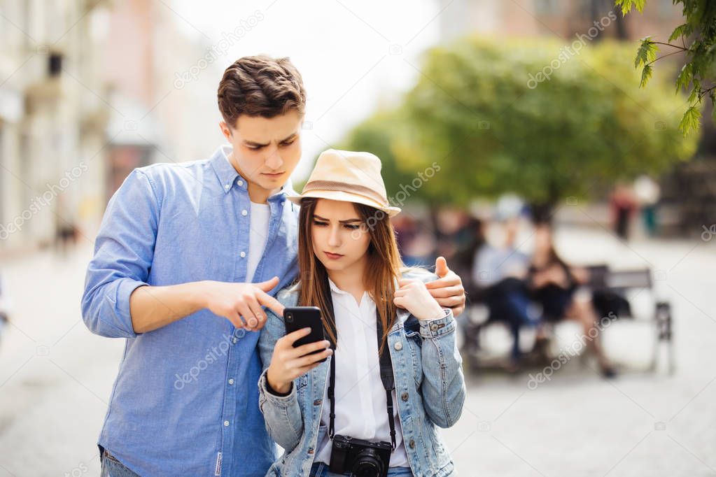 Portrait of young couple of tourist in town using mobile phone in new city.
