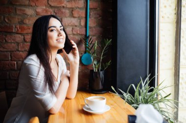 Kafede kahve içme ve cep telefonu üzerinde pencereden bakarak konuşmaya kafede genç kadın