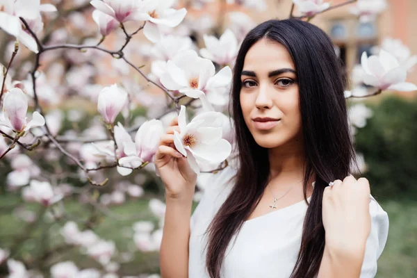 Portréja egy fiatal gyönyörű nő közelében magnólia fát, virágok. — Stock Fotó