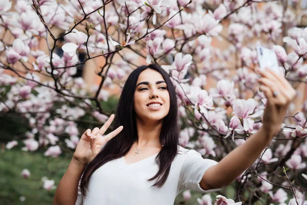 Bella donna caucasica elegante fare selfie in fiore magnolia giardino . — Foto Stock
