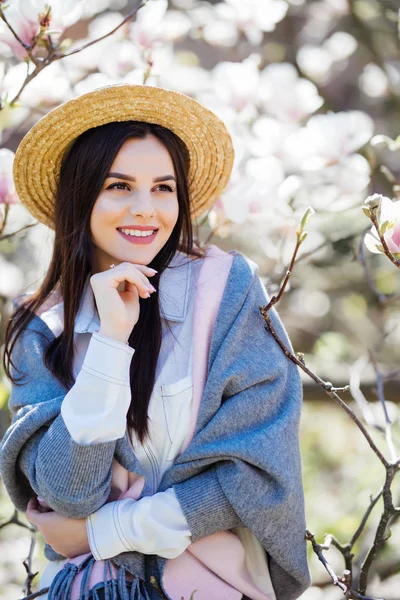 Fiatal gyönyörű lány kaukázusi Szalmakalapot tavasszal virágzó magnólia kertben. — Stock Fotó