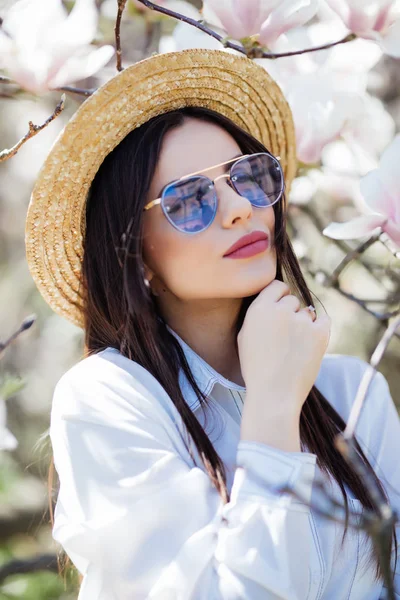 Portrait de belle jeune femme en chapeau d'été et lunettes de soleil avec magnolia arbre de fleurs — Photo