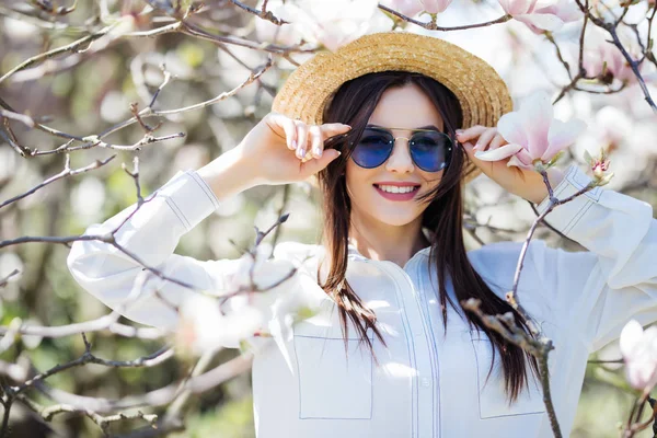 Πορτρέτο του όμορφη νεαρή γυναίκα σε καλοκαιρινό καπέλο και γυαλιά ηλίου με δέντρο magnolia λουλούδια — Φωτογραφία Αρχείου