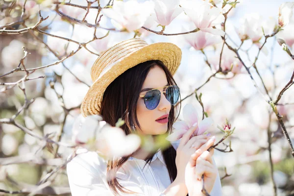 Napszemüveg és szalmakalap áll közel Magnolia virágzó fiatal nő szépségét virágok tavaszi graden fa — Stock Fotó