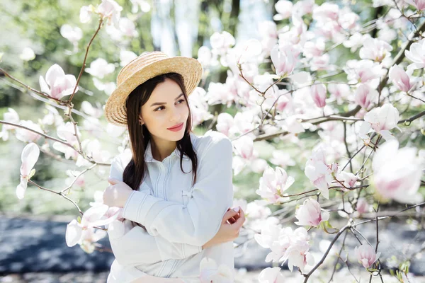 Portrait extérieur de jeune belle femme en chapeau de paille posant près de magnolia arbre à fleurs . — Photo