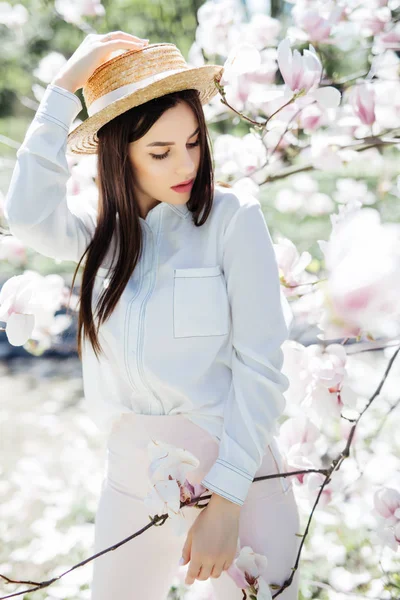 Jeune femme de beauté en chapeau de paille autour magnolia rose arbre de fleurs dans le jardin de printemps — Photo