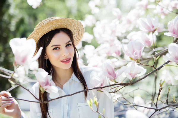 A fiatal szépség nő szalmakalap, ezen a környéken: magnolia fa rózsaszín virágok tavaszi kert — Stock Fotó