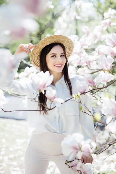 Portrait extérieur de jeune belle femme en chapeau de paille posant près de magnolia arbre à fleurs . — Photo