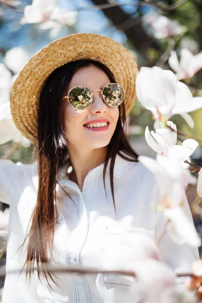 Νέοι όμορφο κορίτσι στο καλοκαιρινό καπέλο και γυαλιά ηλίου Χαλαρώστε στον όμορφο κήπο με ροζ μανόλιες ανθίζοντας δέντρο — Φωτογραφία Αρχείου
