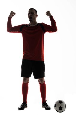 Genç futbol oyuncu zafer çığlık silah kadar beyaz arka plan üzerinde izole futbol topu ile silüeti