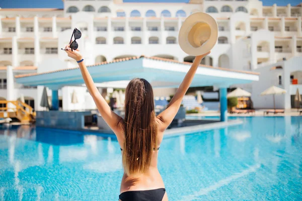 Вид на женщину с поднятыми руками в шляпе и солнцезащитных очках, наслаждающуюся отдыхом в бассейне — стоковое фото