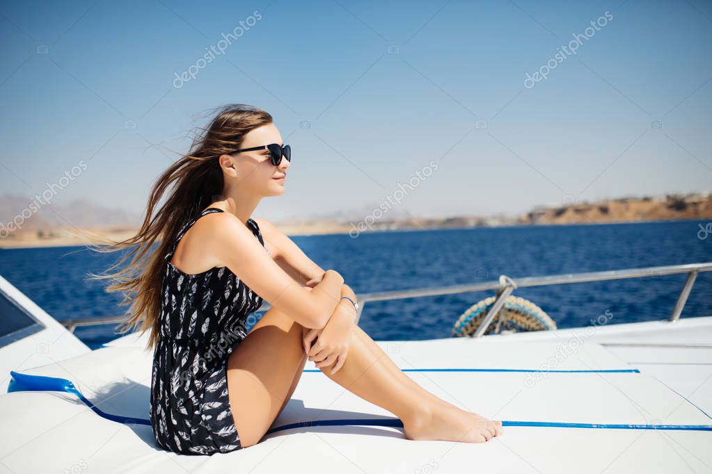 Portrait of young amazing girl in sunglasses wearing hat sitting on the yacht