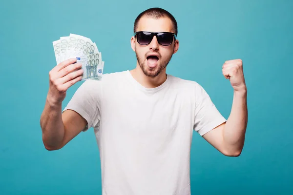 Πορτραίτο ενός άνδρα νέοι καλοκαίρι σε λευκό t-shirt εκμετάλλευση μετρητά χρήματα κραυγή νίκης ενώ χαμογελώντας απομονώνονται σε πράσινο φόντο — Φωτογραφία Αρχείου