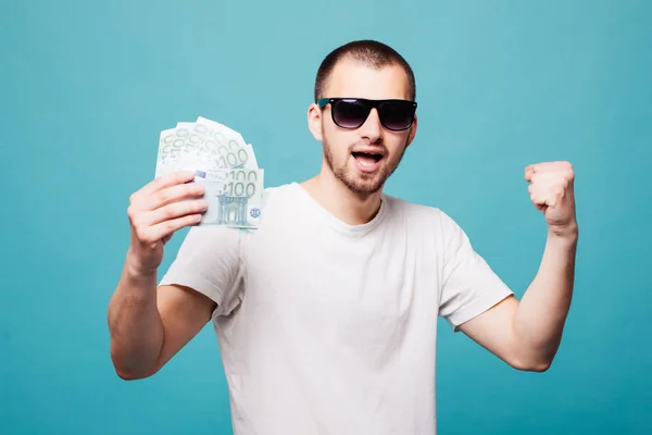 Πορτραίτο ενός άνδρα νέοι καλοκαίρι σε λευκό t-shirt εκμετάλλευση μετρητά χρήματα κραυγή νίκης ενώ χαμογελώντας απομονώνονται σε πράσινο φόντο — Φωτογραφία Αρχείου
