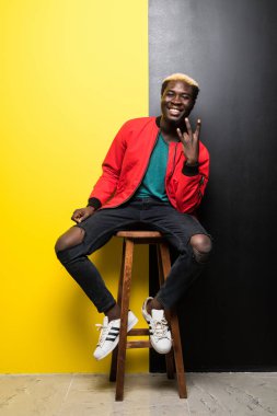 Mutlu genç Afrika adam renk arka plan üzerinde izole bir sandalyede oturuyor