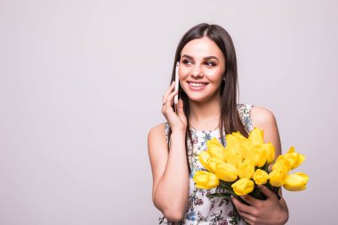 Büyük beyaz bitti izole Sarı laleler buket tutarken cep telefonu üzerinde konuşurken elbiseli mutlu bir genç kız portresi