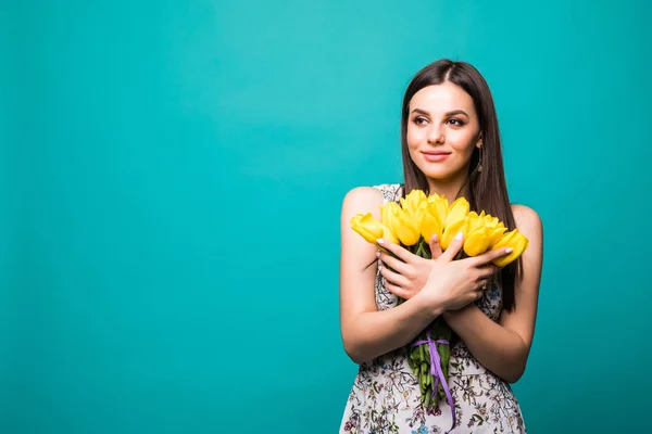 Ritratto di una bella giovane donna in abito ssummer con bouquet di tulipani gialli isolato su sfondo blu — Foto Stock