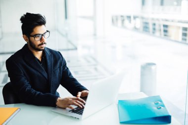 Hintli adam modern ofis içinde laptop üzerinde çalışıyor. Genç iş adamı gözlük iş üstünde laptop