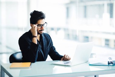 Kağıt okuma, ofiste dizüstü bilgisayar ile internet'te sörf notlar alarak bir meşgul Hint adam multitasking portresi