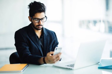 Genç Hintli masasında, iş ofisinde smartphone cep telefonu ile metin okuma şirketin CEO'su