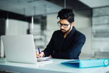Neşeli genç Hintli işadamı not defterinde office Danışma Yazma