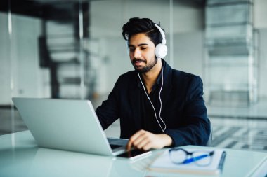 Hintli genç iş adamı earphones ile ofiste çalışmak ve müzik dinlemek dizüstü bilgisayar