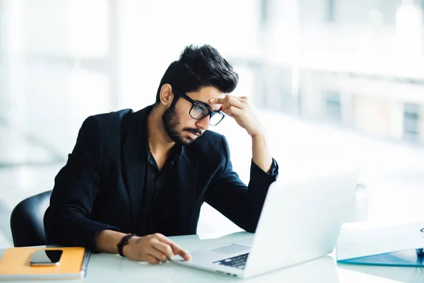 Фото індійські чоловік засмучений, робота, сидячи перед ноутбук в сучасні офісні — стокове фото