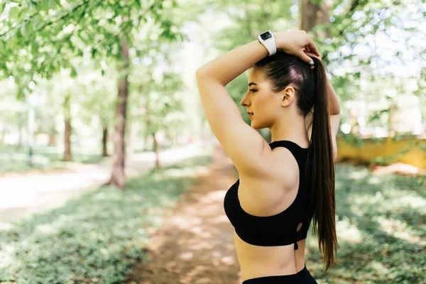 Жінка прив'язує волосся до хвоста, готуючись до занять у парку. Красива молода спортивна жінка прикріплює довге волосся в парку. Усміхнена жінка затягує волосся для бігу в парку . — стокове фото