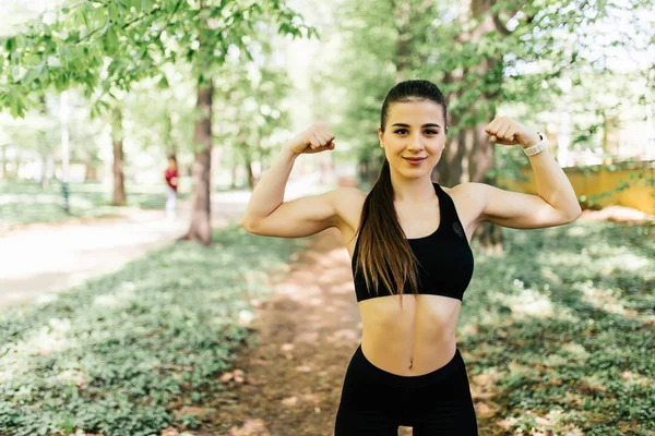 Sport jeune femme avec un corps parfait montrant biceps, fille de remise en forme dans le parc vert — Photo