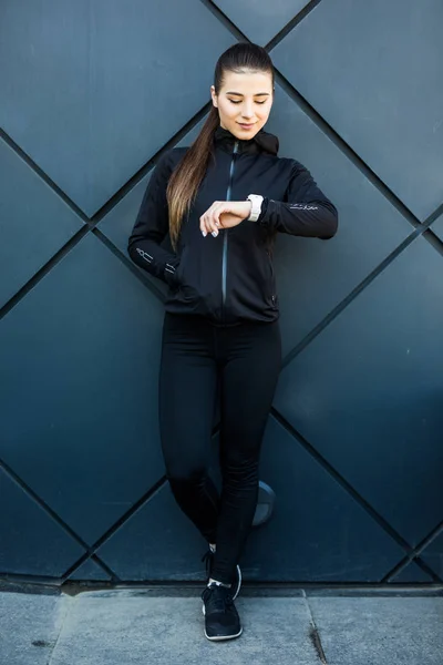 Joven belleza mujer comprueba su smartwatch fuera contra negro calle pared — Foto de Stock