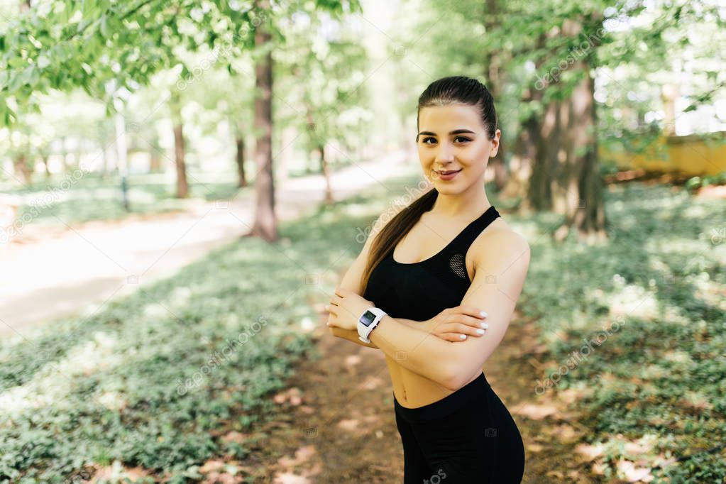 Beautiful and athletic girl with clothes for jogging standing with her hands crossed over her chest and looking at the camera in park