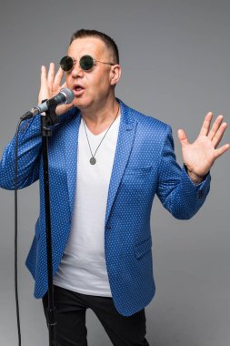 Orta yaş şovmen görüşmeci duygularla. Beyaz arka plan üzerinde mikrofon tutan genç zarif olgun adam. Şovmen kavramı.