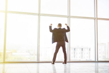 Heyecanlı orta yaş işadamı ile zafer reised eller yukarı Sunset'teki panoramik pencerenin önünde