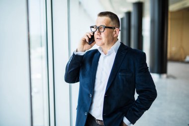 Telefonunuzun ve cityscape bakan pencerenin önünde oturan işadamı orta gülümseyen yaşlı