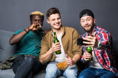 Çekici çocuklar bira içme, akıllı telefon kullanarak ve tv izlerken, evde kanepede otururken gülümseyen selfie yapıyor