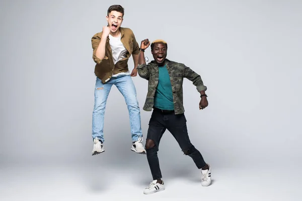 Portret van een twee gemengd ras vrolijke jonge mannen springen en geïsoleerde vieren op witte achtergrond — Stockfoto