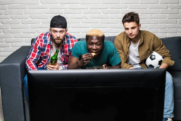 De drie internationale mannen met een biertje en een levensmiddel kijken en een voetbal gebaar — Stockfoto