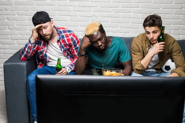 friendship, sports and entertainment concept. Sad male friends with beer watching sports on tv at home