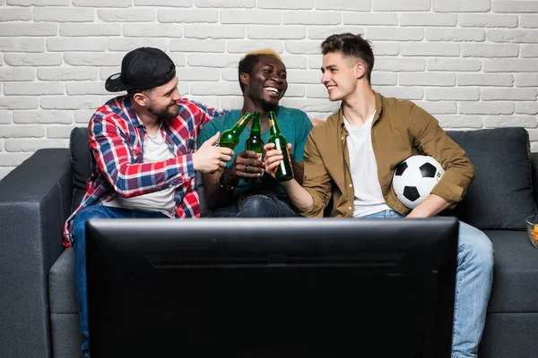 Felices hombres alegres sosteniendo un vaso de cerveza mientras miran la televisión —  Fotos de Stock