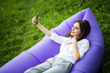 Temiz hava sakin ol. Genç ve güzel kadın güneş Park'ta çimenlerin üzerinde dinlenme sırasında şişme kanepe lamzac kullanım cep telefonu üzerinde yalan