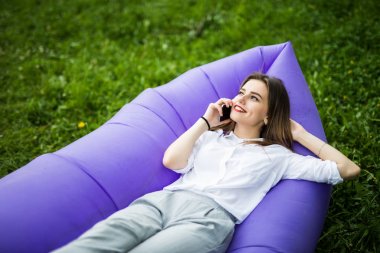 Genç ve güzel kadın şişme kanepe lamzac üzerinde yalan Park çimenlerin üzerinde dinlenme sırasında telefonla konuşmak