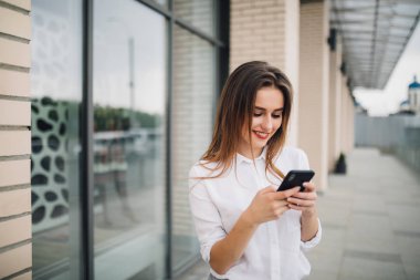 Genç güzel kadın kullanım cep telefonu bir ticari bina önünde onun elinde