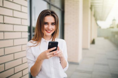 Genç güzel kadın kullanım cep telefonu bir ticari bina önünde onun elinde