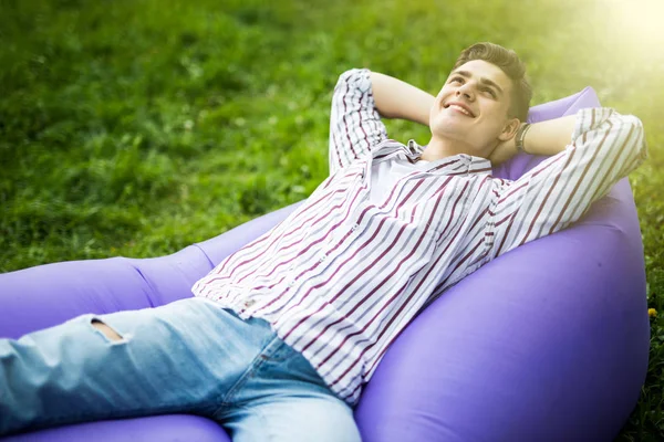 Relaxa. Bonito jovem deitado no sofá inflável lamzac enquanto descansa na grama no parque ao sol — Fotografia de Stock