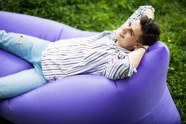 お気軽に。公園の芝生の上で休んでいる間インフレータブルソファ lamzac で横になっているハンサムな若い男 — ストック写真