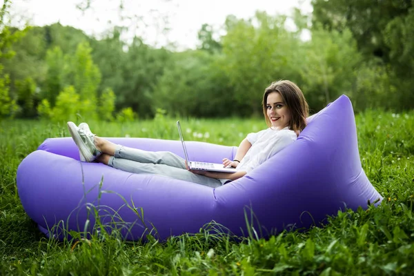 インフレータブルソファ lamzac 参照インターネットでノート パソコンに公園の芝生の上で休んでいる間に横たわるかなり若い女 — ストック写真