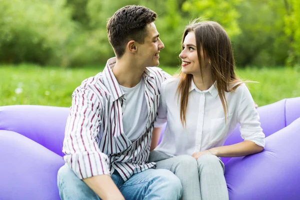 Pareja del amor que miente en el lamzac inflable del sofá en el ordenador portátil mientras que descansa en la hierba en el parque que mira uno al otro y se divierte —  Fotos de Stock