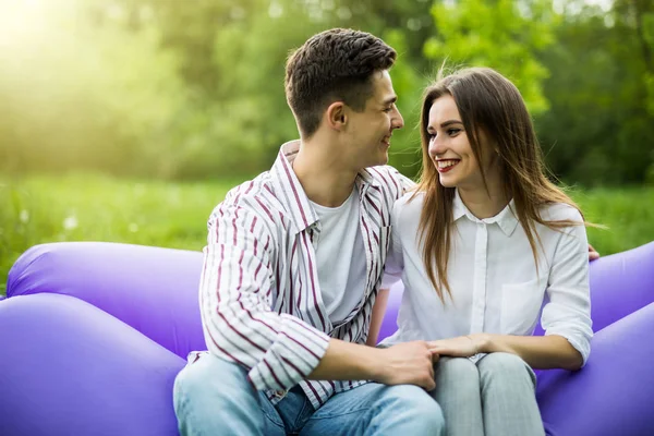 Joven pareja pasar tiempo juntos sentado en el sofá inflable lamzac mientras descansa en la hierba en el parque —  Fotos de Stock