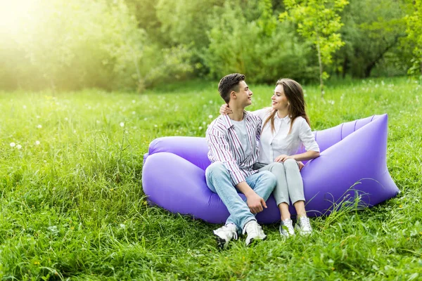 Jeune couple passer du temps ensemble assis sur un canapé gonflable tout en se reposant sur l'herbe dans le parc — Photo