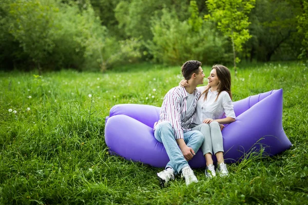 Pareja del amor que miente en el lamzac inflable del sofá en el ordenador portátil mientras que descansa en la hierba en el parque que mira uno al otro y se divierte — Foto de Stock